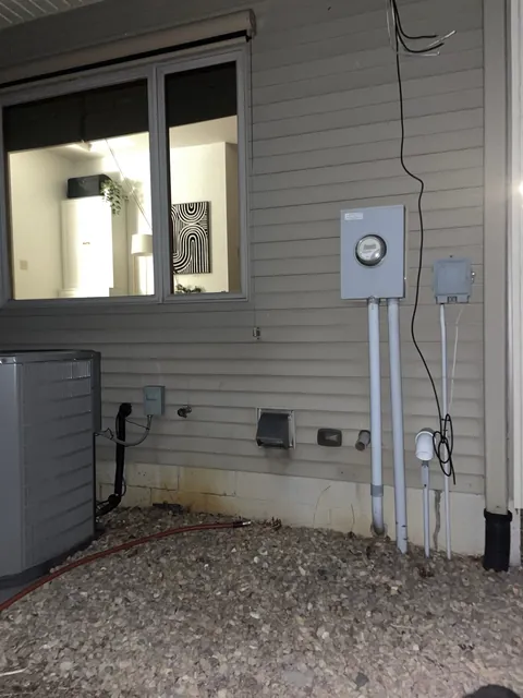 An exterior meter socket and service disconnect mounted on a wall next to an air conditioning condenser.